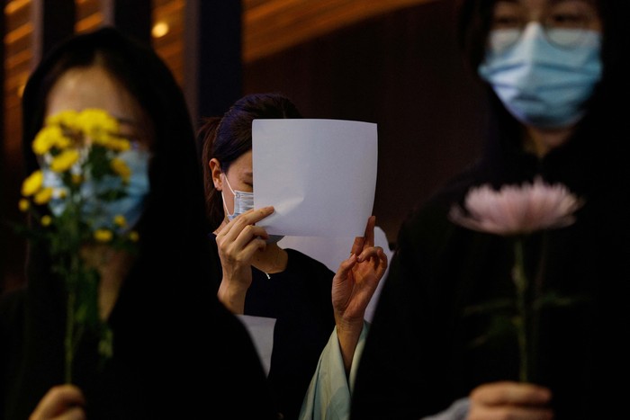 People hold white sheets of paper and flowers in protest over coronavirus disease (COVID-19) restrictions in mainland China, during a commemoration of the victims of a fire in Urumqi, in Hong Kong, China November 28, 2022. REUTERS/Tyrone Siu