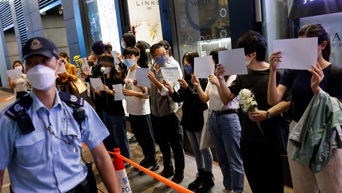 People hold white sheets of paper and flowers in protest over coronavirus disease (COVID-19) restrictions in mainland China, during a commemoration of the victims of a fire in Urumqi, in Hong Kong, China November 28, 2022. REUTERS/Tyrone Siu