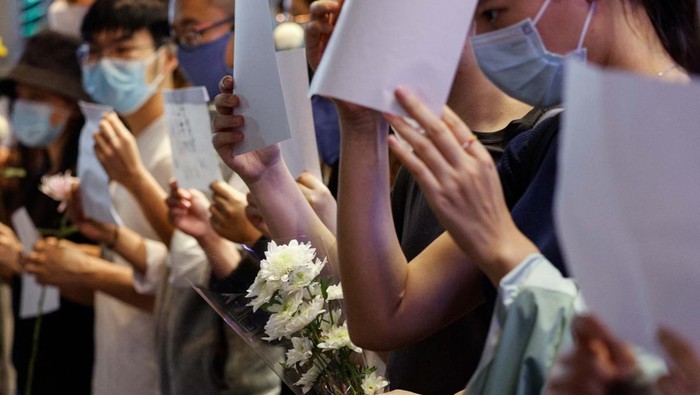 Warga China Demo dengan Kertas Kosong, Apa Maksudnya? People hold white sheets of paper and flowers in protest over coronavirus disease (COVID-19) restrictions in mainland China, during a commemoration of the victims of a fire in Urumqi, in Hong Kong, China November 28, 2022. REUTERS/Tyrone Siu