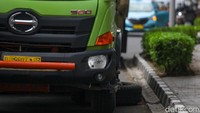 Di sekitar truk itu, terlihat 1 ban serep tergeletak di samping truk beserta 1 buah dongkrak di bawah badan truk.
