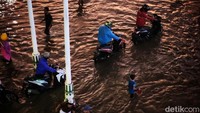 Pemotor memilih untuk menuntun kendaraannya saat menerobos genangan banjir.