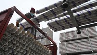 Pekerja memindahkan pipa dari mobil truk ke forklift.