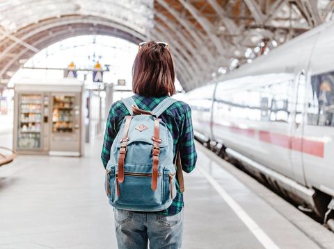 A young tourist girl with backpack waits for train on railway station
