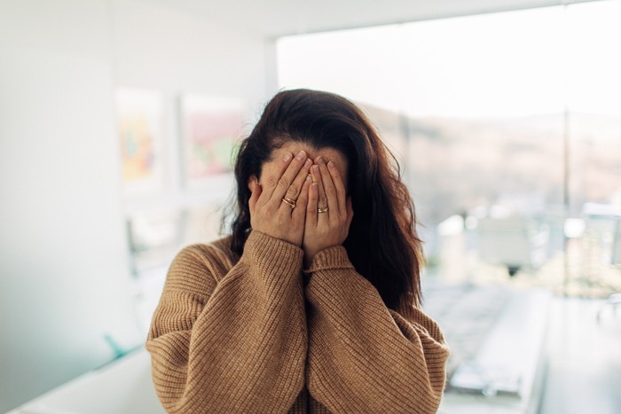 Portrait of a shy young woman in her loft apartment, covering her face with her hands