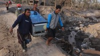 Warga terdampak awan panas guguran Gunung Semeru tetap menyelamatkan barang berharga dari rumah mereka yang rusak dan tertimbun abu vulkanik. (Suryanto/Getty Images)