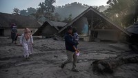 Orang-orang berjalan melewati rumah-rumah yang terendam abu dan lumpur setelah letusan Gunung Semeru di desa Kajar Kuning, Lumajang, Jawa Timur, Senin (5/12/2022). (Juni Kriswanto/AFP/Getty Images)