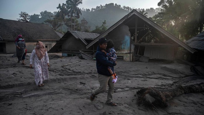 Rumah-rumah Warga Tertimbun Abu Vulkanik Gunung Semeru People walk past homes covered with ash and mud following a volcanic eruption by Mount Semeru at Kajar Kuning village in Lumajang on December 5, 2022. - Indonesia's Mount Semeru erupted on December 4 spewing hot ash clouds a mile high and rivers of lava down its side while sparking the evacuation of nearly 2,000 people exactly one year after its last major eruption killed dozens. (Photo by JUNI KRISWANTO / AFP) (Photo by JUNI KRISWANTO/AFP via Getty Images)