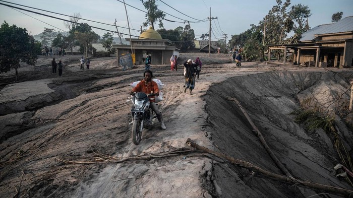Rumah-rumah Warga Tertimbun Abu Vulkanik Gunung Semeru People walk past homes covered with ash and mud following a volcanic eruption by Mount Semeru at Kajar Kuning village in Lumajang on December 5, 2022. - Indonesia's Mount Semeru erupted on December 4 spewing hot ash clouds a mile high and rivers of lava down its side while sparking the evacuation of nearly 2,000 people exactly one year after its last major eruption killed dozens. (Photo by JUNI KRISWANTO / AFP) (Photo by JUNI KRISWANTO/AFP via Getty Images)