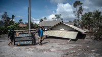 Dua orang warga memikul lemari melintasi jalanan yang diselimuti material vulkanik di Desa Kajar Kuning. Juni Kriswanto/AFP/Getty Images.