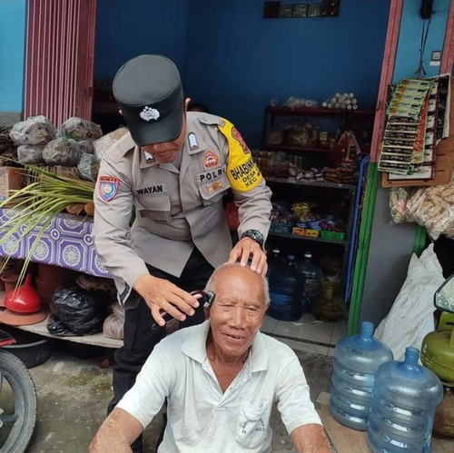 Bripka I Wayan Wendi Raharja Bhabinkamtibmas Desa Cemagi, Kabupaten Badung, Bali, saat mencukur rambut lansia di desa setempat secara gratis, Rabu (7/12/2022).