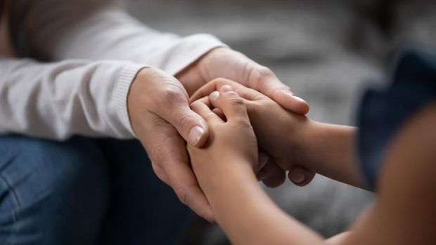 Close up compassionate young foster parent holding hands of little kid girl, giving psychological help, supporting at home. Sincere different generations family sharing secrets or making peace.