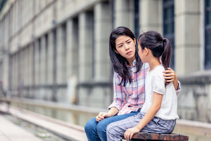 A woman is holding her arm around a young girl and is looking serious.