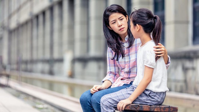 A woman is holding her arm around a young girl and is looking serious.