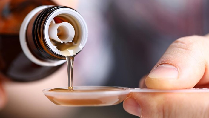 Sick man holding in hands vial with syrup close-up. Seasonal disease prevention and treatment or supplement and food additives with vitamins and omega 3 concept