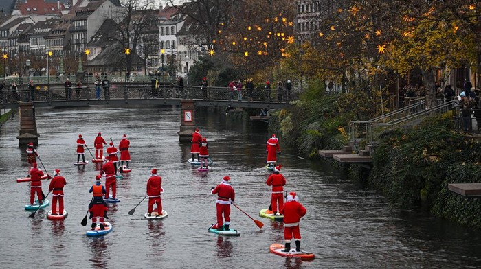 Sambut Natal, Rombongan Sintreklas Dayung Papan di Sungai Prancis Pestrians take picture of paddlers dressed as Santa Claus as they attend a SUP (Stand Up Paddleboarding) parade on the Ill river in Strasbourg, eastern France, on December 3, 2022. (Photo by SEBASTIEN BOZON / AFP) (Photo by SEBASTIEN BOZON/AFP via Getty Images)