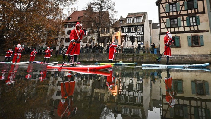 Pestrians take picture of paddlers dressed as Santa Claus as they attend a SUP (Stand Up Paddleboarding) parade on the Ill river in Strasbourg, eastern France, on December 3, 2022. (Photo by SEBASTIEN BOZON / AFP) (Photo by SEBASTIEN BOZON/AFP via Getty Images)