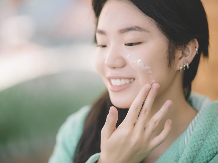 an asian chinese teenager girl applying moisturiser facial cream on hand and face