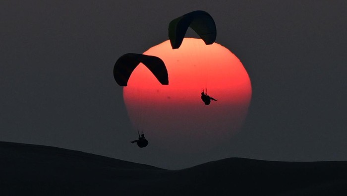 7 Wisata di Doha yang Bisa Dijajal Selain Nonton Piala Dunia Paragliders float over a sand dune during sunset at the Sealine Beach Resort in Doha on December 6, 2022, during the Qatar 2022 World Cup football tournament. (Photo by OZAN KOSE / AFP) (Photo by OZAN KOSE/AFP via Getty Images)
