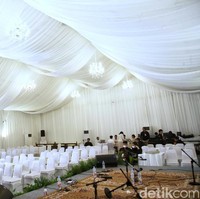 Tenda itu tampak terpasang di jalanan depan rumah Erina, lengkap dengan backdrop warna putih di masing-masing sisi.