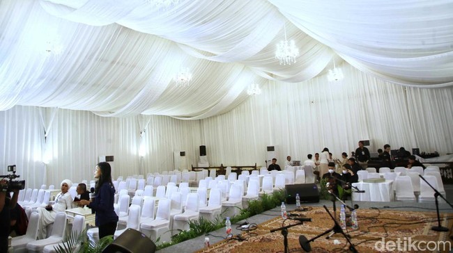 Tenda itu tampak terpasang di jalanan depan rumah Erina, lengkap dengan backdrop warna putih di masing-masing sisi.