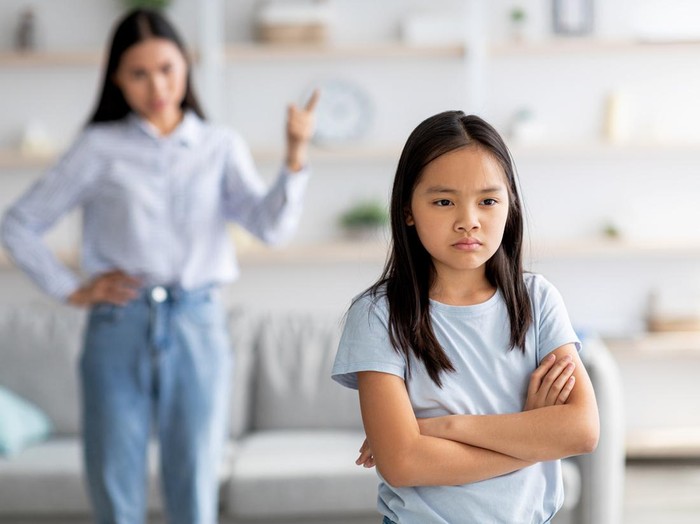 Family conflict. Mother and daughter quarreling at home, sulky child girl ignoring her mom, standing back to her with crossed arms, selective focus, copy space