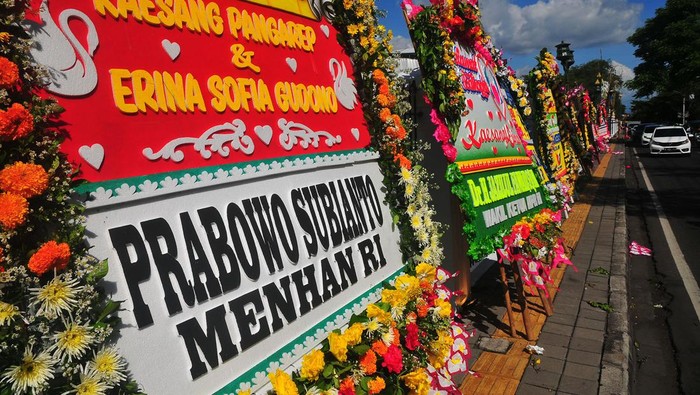 Pengendara motor melintas di dekat sejumlah karangan bunga ucapan selamat atas pernikahan putra Presiden Joko Widodo, Kaesang Pangarep dengan Erina Gudono di kawasan Pura Mangkunegaran, Solo, Jawa Tengah, Sabtu (10/12/2022). Kiriman karangan bunga tersebut datang dari sejumlah pejabat tinggi negara hingga pejabat daerah.