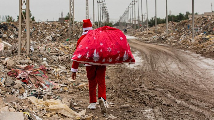 Anak-anak di Daerah Kumuh Irak Sambut Kedatangan ’Sinterklas’ Mohamed Maarouf, 28, while dressed in Saint Nicholas (Santa Claus) costume, distributes Christmas gifts to impoverished children living in slums near the centre of Iraq's southern city of Basra. (Photo by Hussein FALEH / AFP) (Photo by HUSSEIN FALEH/AFP via Getty Images)