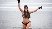 Seorang wanita yang mengenakan bikini, berenang di danau yang tertutup es.