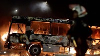 Polisi berjaga di depan bus yang terbakar.