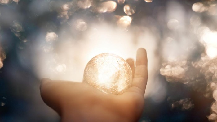 unrecognizable witch hand holding magic globe, defocused lights in background.