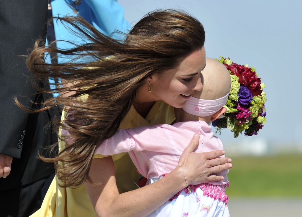 Catherine, the Duchess of Cambridge is presented with flowers and a hug by 6-year-old Diamond Marshall on arrival with Prince William at Calgary International Airport in Calgary on July 7, 2011. The Make-a-Wish Foundation arranged for Marshall, a cancer patient, to greet the royal couple.  AFP PHOTO / Pool / Todd KOROL (Photo credit should read TODD KOROL/AFP via Getty Images)