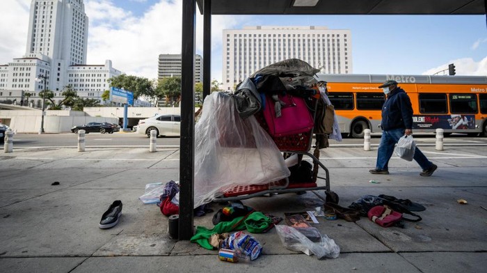 Los Angeles, CA - December 12:A man walks past a homeless persons belongings under a Metro bus shelter just blocks from Los Angeles City Hall on Monday, December 12, 2022. LA Mayor Karen Bass declared a state of emergency on homelessness as her first