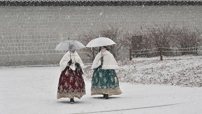 Visitors wearing traditional hanbok dress walk through Gyeongbokgung palace during snowfall in central Seoul on December 15, 2022. (Photo by Jung Yeon-je / AFP) (Photo by JUNG YEON-JE/AFP via Getty Images)