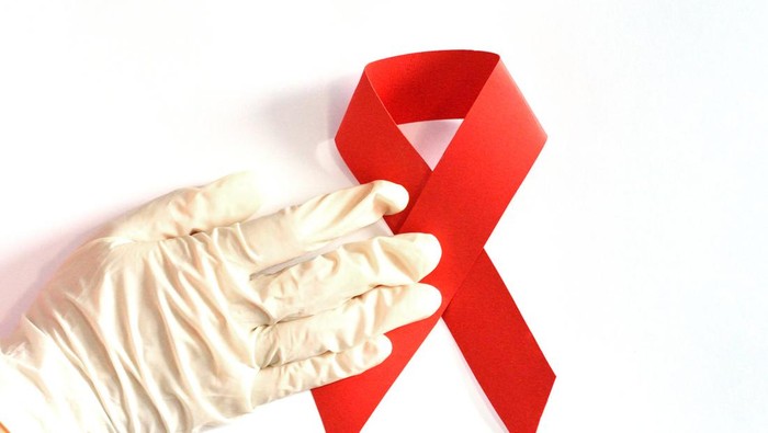 Human hand in protective glove holding red ribbon, HIV.