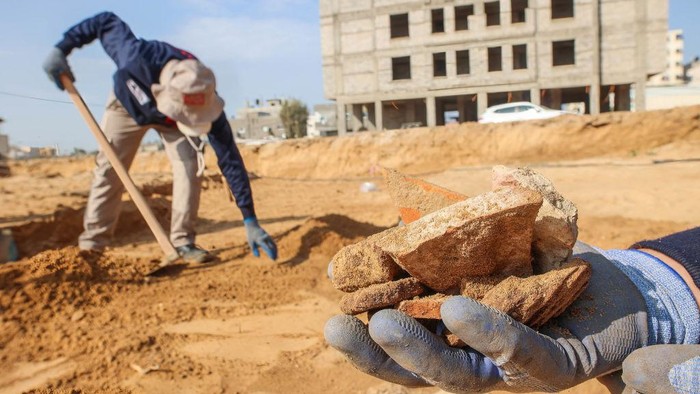 63 Makam Era Romawi Kuno Ditemukan di Gaza GAZA, PALESTINE - 2022/12/15: A Palestinian worker carries artefacts of pottery found inside a newly discovered Roman-era cemetery in the Gaza Strip. Hamas authorities in Gaza announced the discovery of over 60 tombs in the ancient burial site. Work crews have been excavating the site since it was discovered last January during preparations for an Egyptian-funded housing project. (Photo by Ahmed Zakot/SOPA Images/LightRocket via Getty Images)