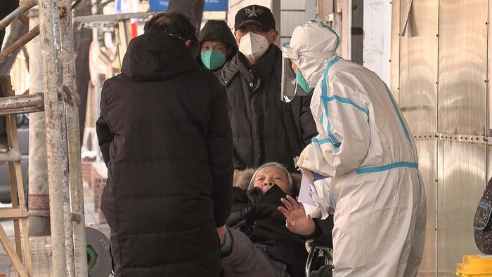 This frame grab from AFPTV video footage shows an elderly woman being assisting by a health worker and a man as she waits outside a fever clinic amid the Covid-19 pandemic in Beijing on December 14, 2022. (Photo by Yuxuan ZHANG / various sources / AFP) (Photo by YUXUAN ZHANG/AFPTV/AFP via Getty Images)