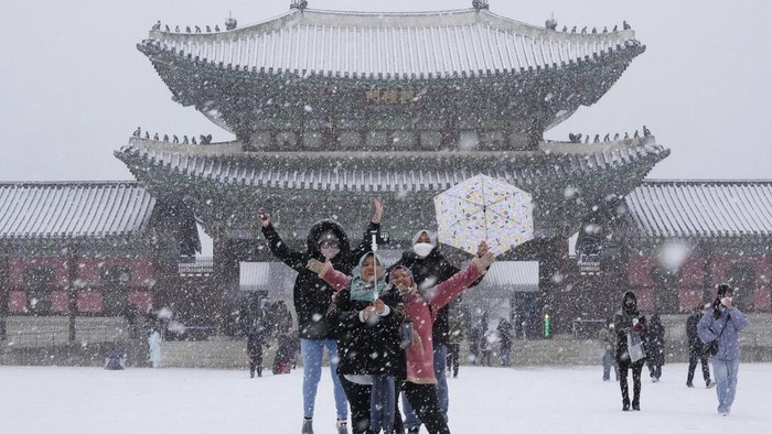 Visitors take a selfie in the snow at the Gyeongbok Palace, the main royal palace during the Joseon Dynasty, and one of South Korea's well known landmarks in Seoul, South Korea. Thursday, Dec. 15, 2022. (AP Photo/Ahn Young-joon)