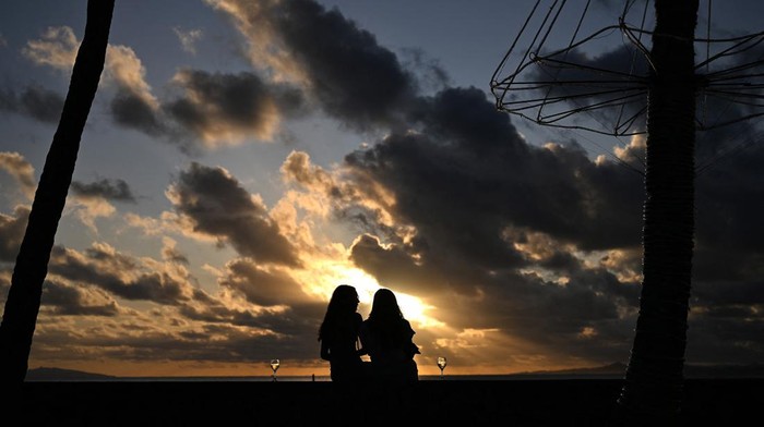 Sunset di Fiji People are silhouetted against the setting sun as they spend their evening at the sea side in Suva on December 16, 2022. (Photo by SAEED KHAN / AFP) (Photo by SAEED KHAN/AFP via Getty Images)