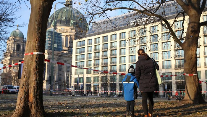 BERLIN, GERMANY - DECEMBER 16: A mother and child look at the scene of a broken giant aquarium, on December 16, 2022 in Berlin, Germany. The aquarium, located in the Radisson Hotel in the Domaquarée complex, spilled approximately 1,500 exotic fish and pushed debris from the hotel’s lobby out onto a heavy pedestrian and traffic thoroughfare when it burst in the early morning. The owners claim the aquarium, which houses the hotel’s central guest elevator and flooded the hotel with one million liters (264,172 gallons) when it broke, is the world's largest freestanding cylindrical one at 14 meters (46 feet) in height. (Photo by Adam Berry/Getty Images)