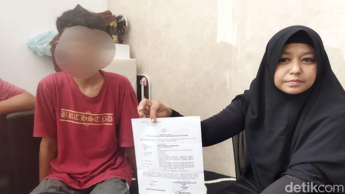Korban bersama ibunya menunjukan surat laporan pengeroyokan di Polsek Bululawang, Malang