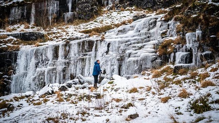 Potret Menakjubkan Air Terjun di Wales yang Membeku People look at icicle formations a frozen waterfall in the Brecon Beacons National Park, Wales. Snow and ice have swept across parts of the UK, with cold wintry conditions set to continue for days. Picture date: Saturday December 17, 2022. (Photo by Ben Birchall/PA Images via Getty Images)