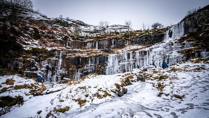 Potret Menakjubkan Air Terjun di Wales yang Membeku People look at icicle formations a frozen waterfall in the Brecon Beacons National Park, Wales. Snow and ice have swept across parts of the UK, with cold wintry conditions set to continue for days. Picture date: Saturday December 17, 2022. (Photo by Ben Birchall/PA Images via Getty Images)