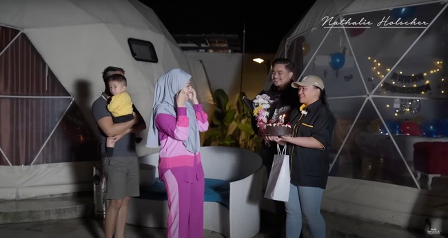 Tak lama setelahnya adik Nathalie datang sambil membawa kue, bunga, dan kado untuk Nathalie. Nathalie pun tampak terkejut mendapat kejutan tersebut. Foto: YouTube/Nathalie Holscher