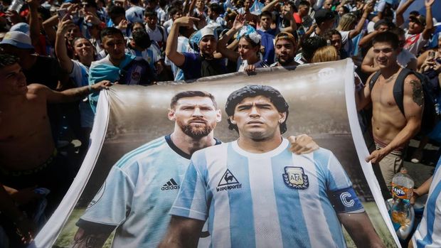 TOPSHOT - Fans of Argentina hold a flag depicting Argentine football stars Lionel Messi (L) and late Diego Maradona (R) while gathering at the Obelisk to celebrate winning the Qatar 2022 World Cup against France in Buenos Aires, on December 18, 2022. (Photo by Emiliano Lasalvia / AFP) (Photo by EMILIANO LASALVIA/AFP via Getty Images)