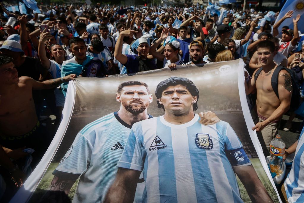 Fans Argentina memegang bendera bergambar bintang sepak bola Argentina Lionel Messi (kiri) dan mendiang Diego Maradona (kanan) saat berkumpul di Obelisk untuk merayakan kemenangan Piala Dunia Qatar 2022 melawan Prancis di Buenos Aires, Argentina, Minggu (18/12/2022). Argentina menjadi juara Piala Dunia 2022 setelah menang adu penalti atas Prancis 4-2. (Photo by EMILIANO LASALVIA/AFP via Getty Images)