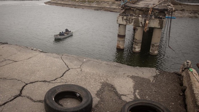 KHARKIV, UKRAINE - DECEMBER 18: After Russian forces retreated from the area and destroyed the reservoir bridge, residents carry goods across the water by a free small taxi boat on December 18, 2022 in Staryi Saltiv, Kharkiv, Ukraine. Kharkiv, Ukraine's second city, was left without power for hours on Friday after the latest attack by Russia on the region's energy infrastructure. The city's mayor said it suffered 