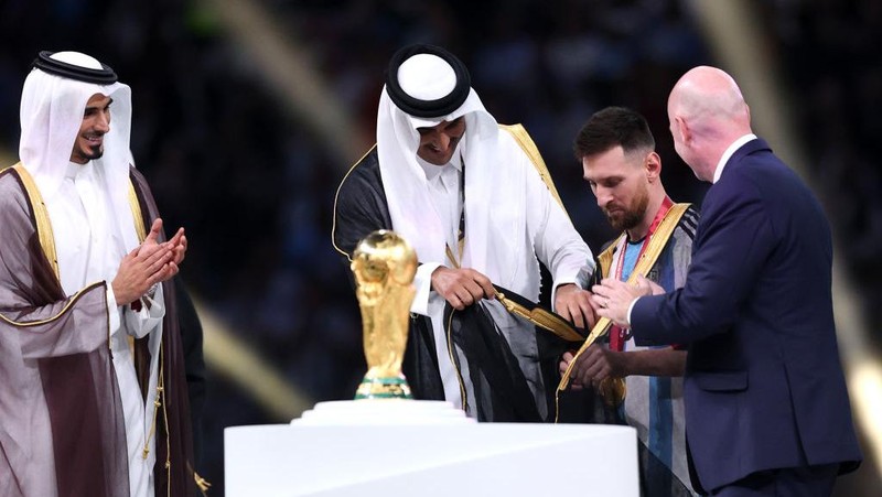 LUSAIL CITY, QATAR - DECEMBER 18: Lionel Messi of Argentina is presented a traditional robe by Sheikh Tamim bin Hamad Al Thani, Emir of Qatar, while Gianni Infantino, President of FIFA, looks on during the awards ceremony after the FIFA World Cup Qatar 2022 Final match between Argentina and France at Lusail Stadium on December 18, 2022 in Lusail City, Qatar. (Photo by Julian Finney/Getty Images)