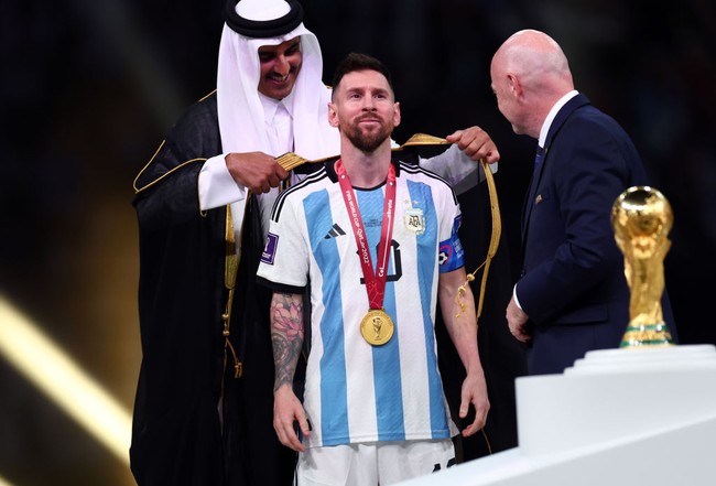 Setelah sukses menyabet gelar juara Piala Dunia 2022, Lionel Messi dan tim Albicelestes melakukan penyerahan trofi yang jadi perhatian. Dalam momen tersebut, Messi dipakaikan jubah hitam khas Arab yang menuai perdebatan. Foto: Getty Images/Amin Mohammad Jamali