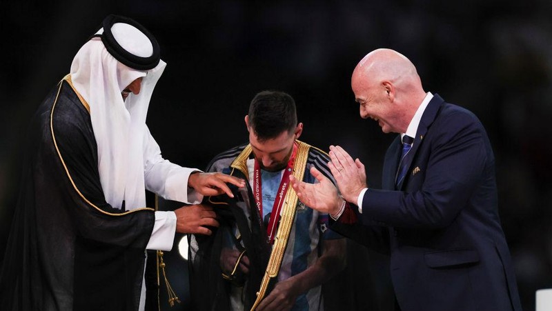 LUSAIL CITY, QATAR - DECEMBER 18:  Lionel Messi of Argentina is presented a traditional black bisht robe by Sheikh Tamim bin Hamad Al Thani, Emir of Qatar, while Gianni Infantino, President of FIFA, looks on after the FIFA World Cup Qatar 2022 Final match between Argentina and France at Lusail Stadium on December 18, 2022 in Lusail City, Qatar. (Photo by Ian MacNicol/Getty Images)