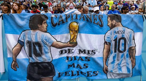 LUSAIL, QATAR - NOVEMBER 22: Detail of a Argentina flag featuring Diego Maradona handing the FIFA World Cup trophy to Lionel Messi alongside Argentina fans in the stands during the FIFA World Cup Qatar 2022 Group C match between Argentina (1) and Saudi Arabia (2) at Lusail Stadium on November 22, 2022 in Lusail City, Qatar. (Photo by Simon Bruty/Anychance/Getty Images)
